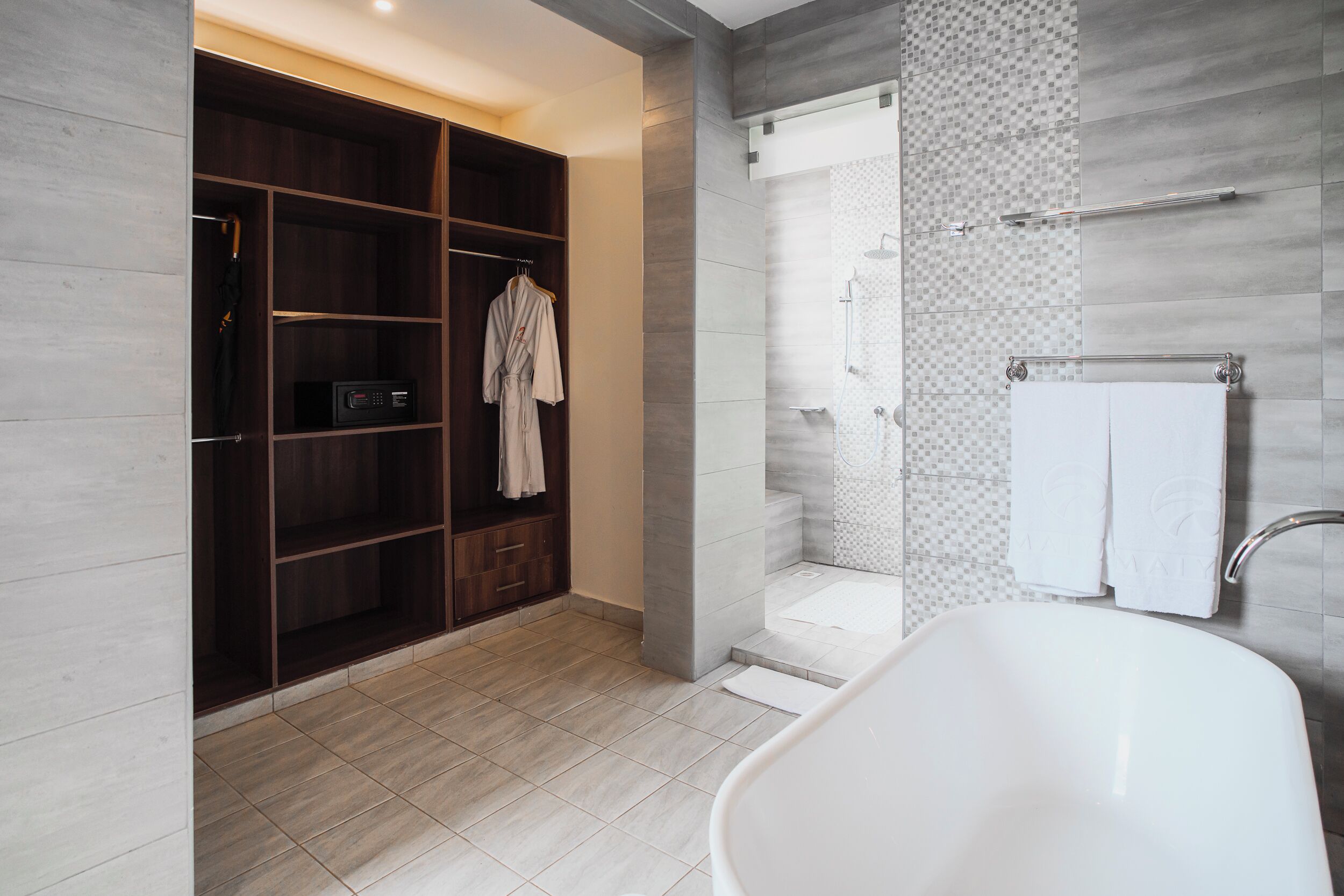 A modern bathroom with a freestanding bathtub, a walk-in shower, and a walk-in closet with hanging robes.