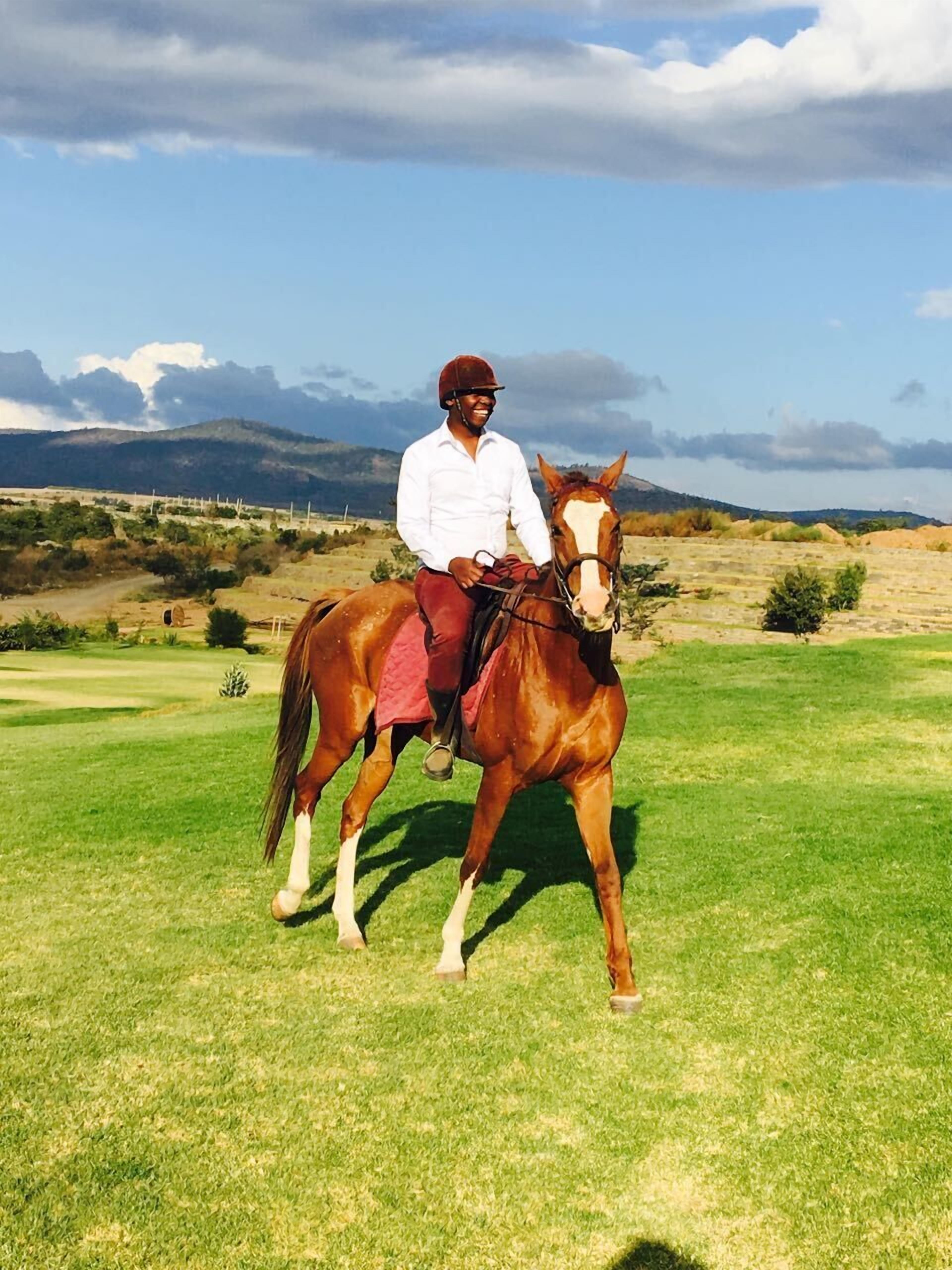 A person riding a horse on a grassy field with mountains in the background.