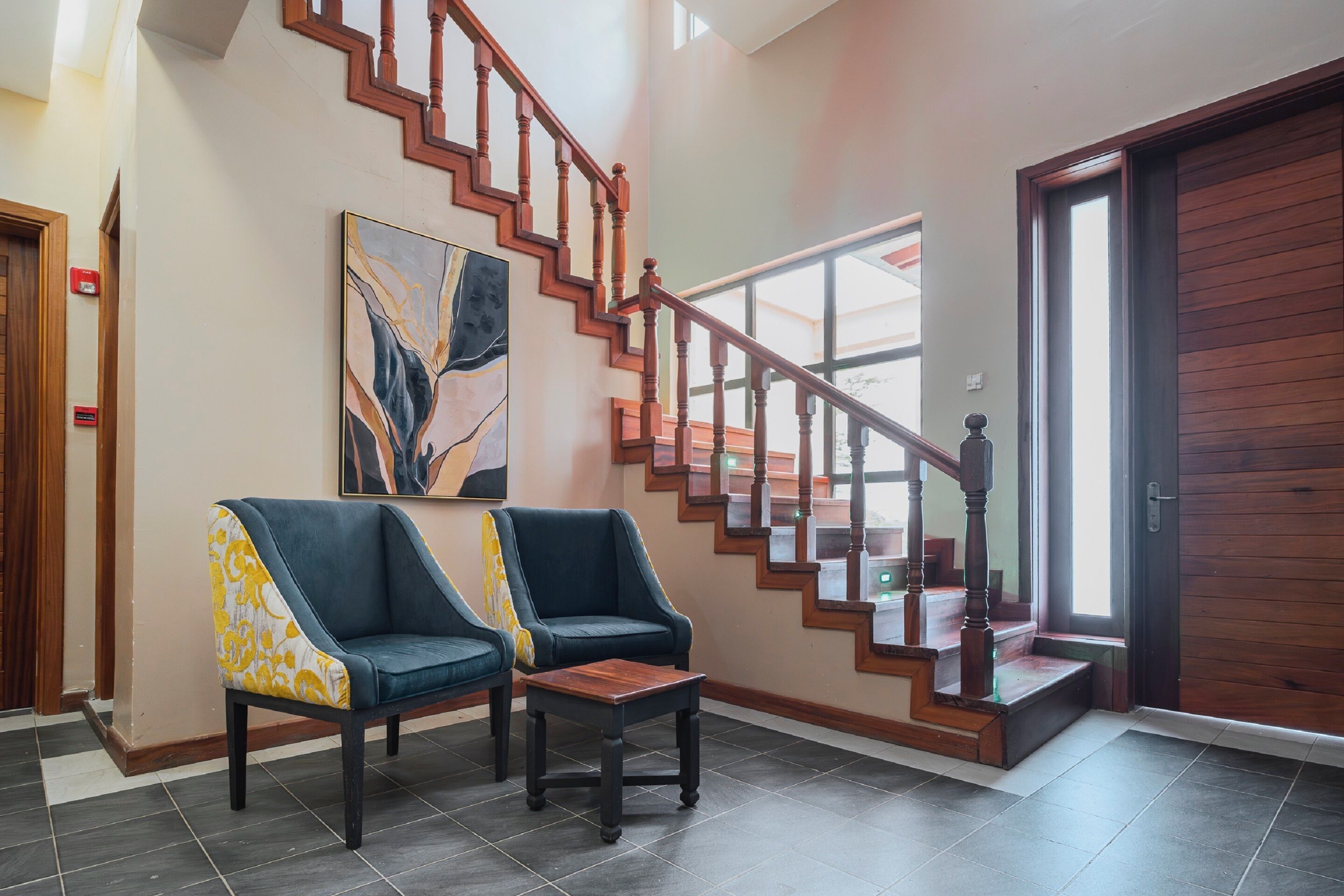 A lobby with a staircase, two armchairs, a small table, and a painting on the wall.