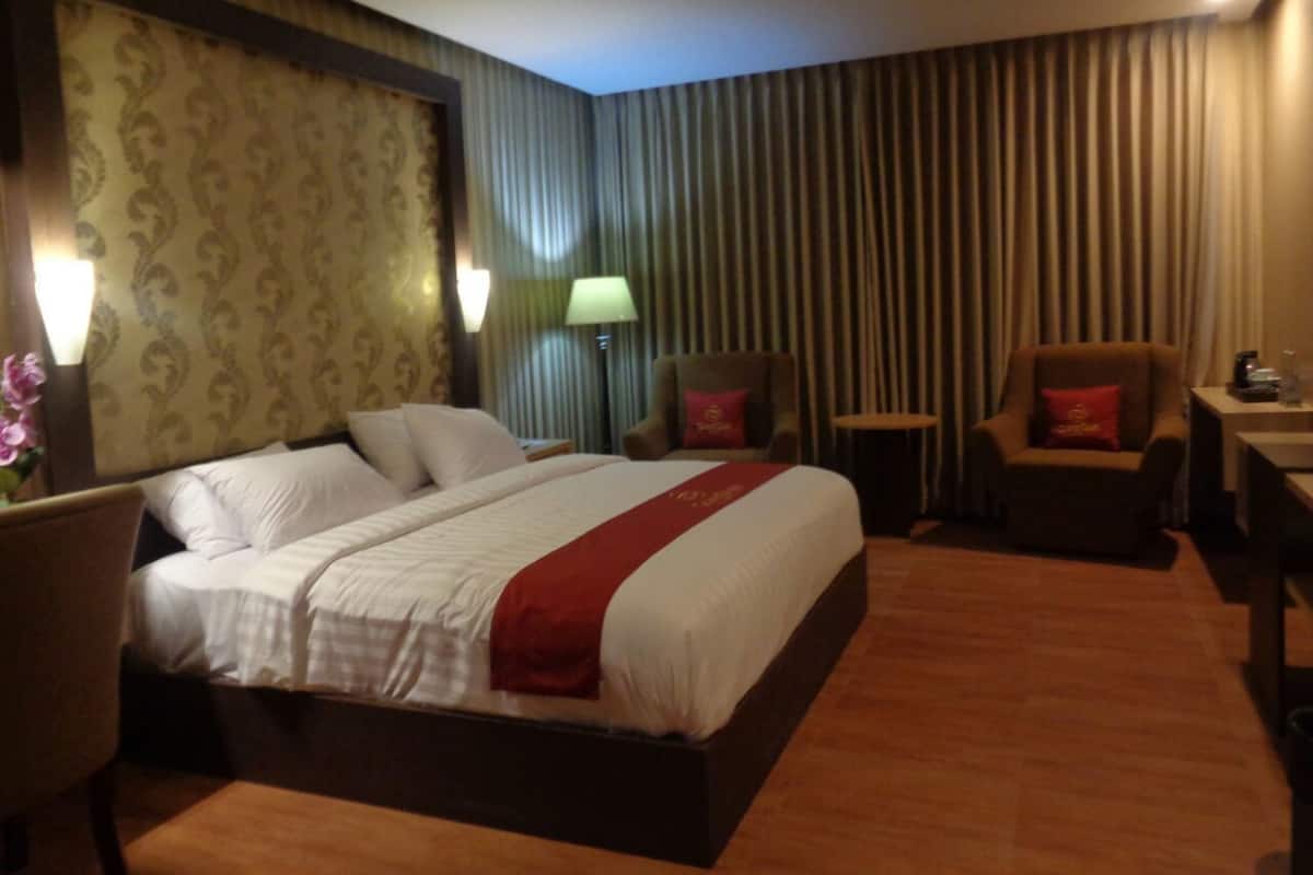 Una habitación de hotel con una cama grande, dos sillas, una mesita y una lámpara.