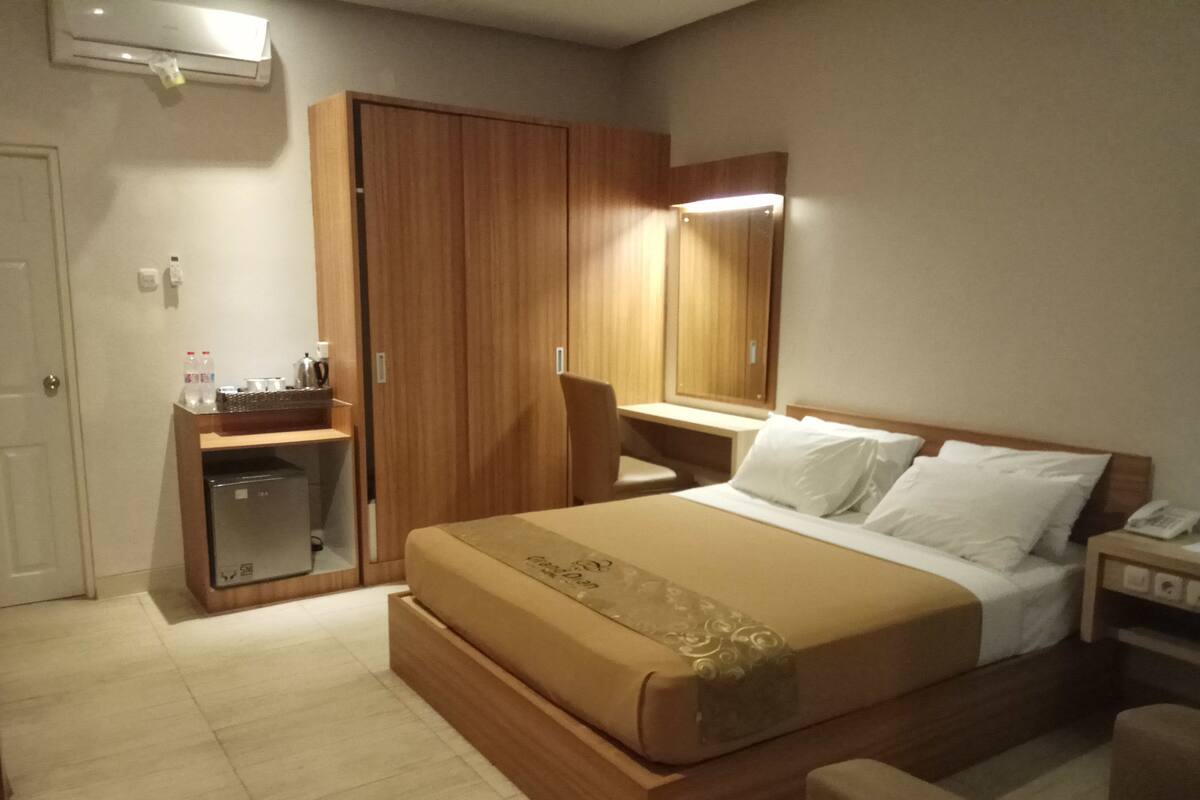 Una habitación de hotel con cama, escritorio, silla, armario y espejo.