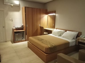 Una habitación de hotel con cama, escritorio, silla, armario y espejo.