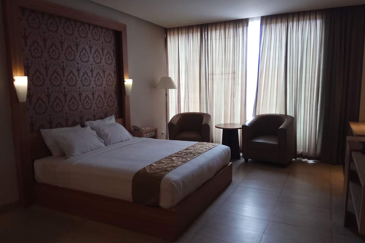 Una habitación de hotel con una cama grande, dos sillones, una mesita y una lámpara.