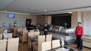 Un restaurant avec des meubles en osier, un espace buffet et un téléviseur fixé au mur.