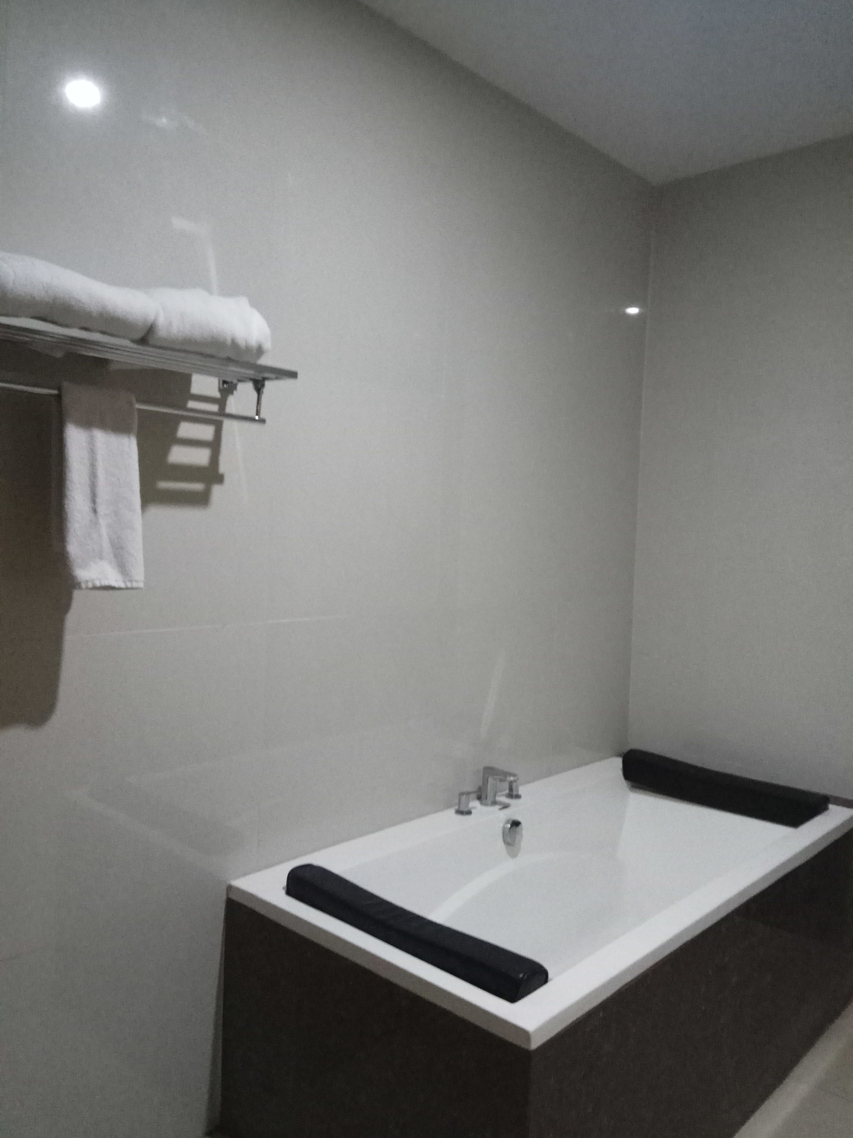Un bagno moderno con una vasca da bagno ampia, un porta asciugamani con un asciugamano piegato e un piccolo ripiano con articoli da toilette.