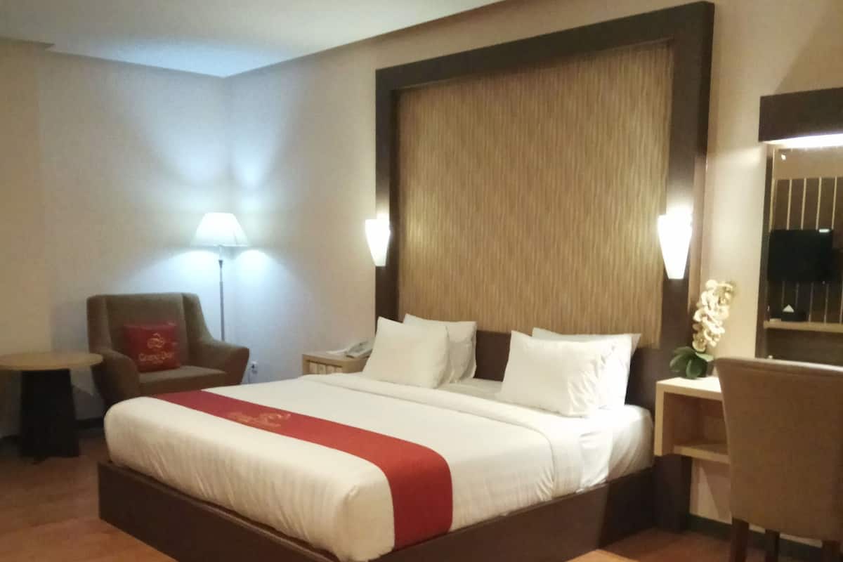 Habitación de hotel con una cama grande, un escritorio, una silla, una lámpara y una mesita de noche.