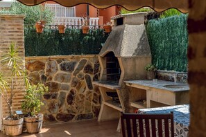 Un patio al aire libre con pared de piedra, una parrilla empotrada, plantas en macetas y suelo de baldosas.