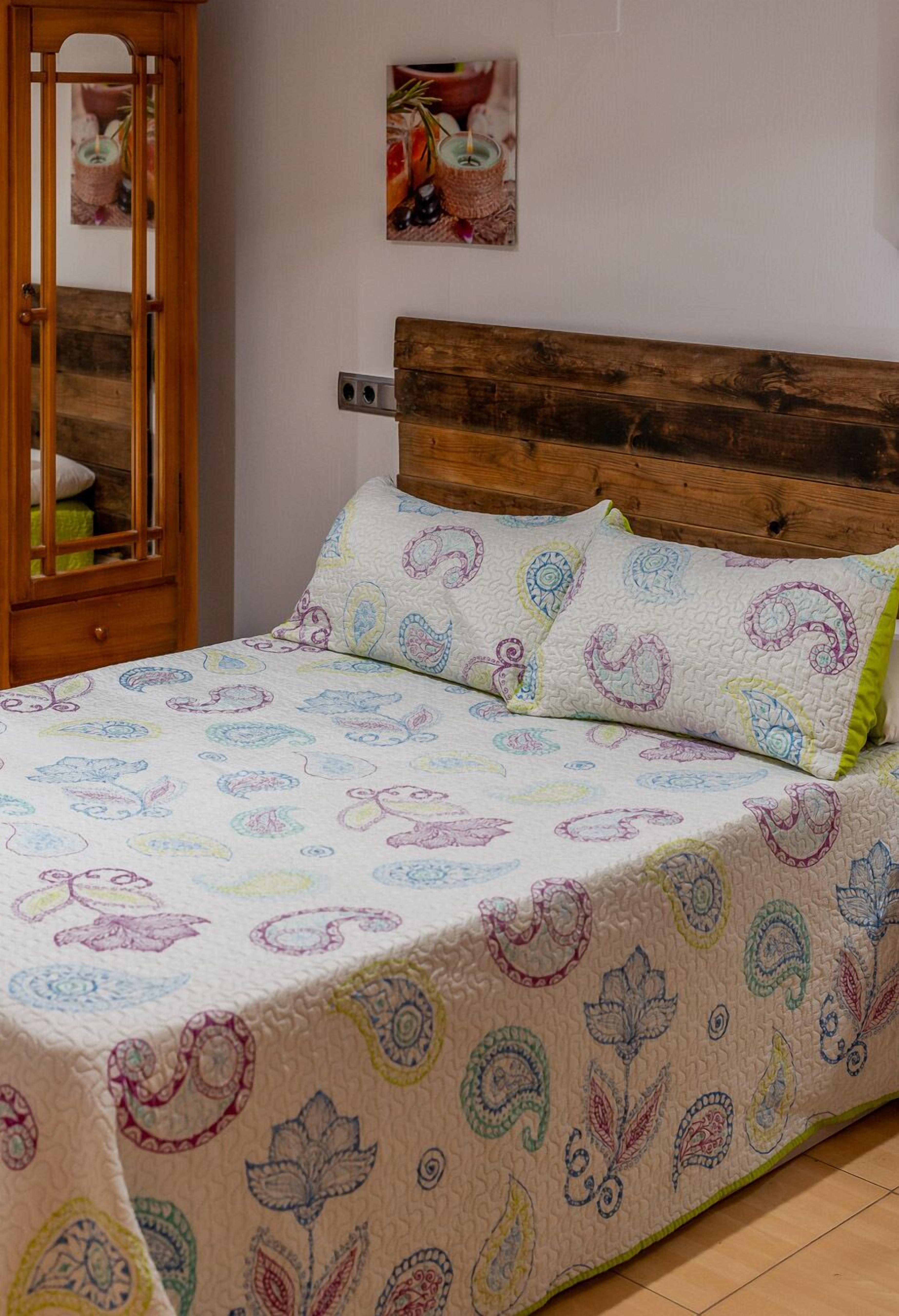 Un lit avec une couvre-lit à motifs, une tête de lit en bois et une table de chevet avec une lampe.
