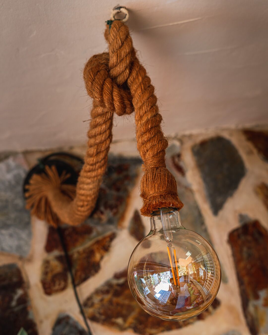 A clear glass bottle with a braided rope handle, suspended from a ceiling hook.