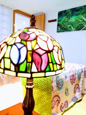 Una lámpara de vitral con un motivo floral, una mesa de madera y una cama con colcha estampada.