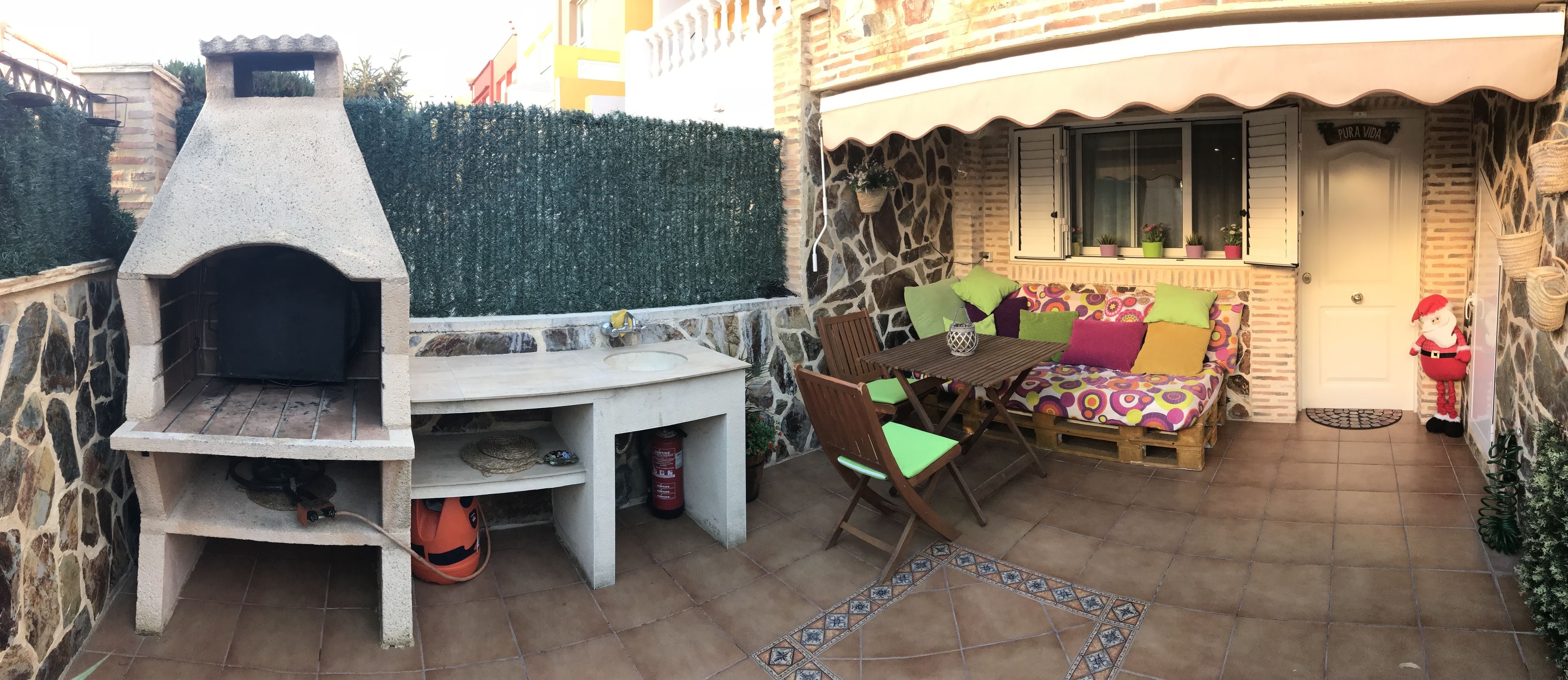 An outdoor patio with a stone oven, seating area with cushions, and a small Christmas tree.
