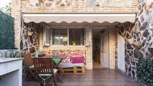 Un rincón exterior acogedor con pared de piedra, banco de madera y una mesa con sillas.