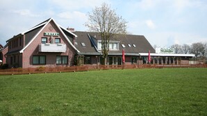 A hotel with a prominent 'HOTEL' sign, a large lawn in front, and a restaurant named 'Lindyhausen Fokke' in the background. - Landgasthaus Fecht (Aurich)