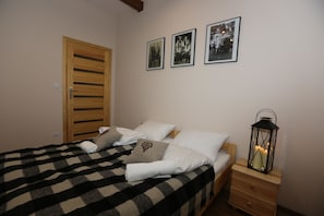 A neatly made bed with a checkered blanket, white pillows, and a decorative pillow. There is a wooden nightstand with a lantern beside the bed. - Maryna House - Apartament Tradycyjny (Zakopane)