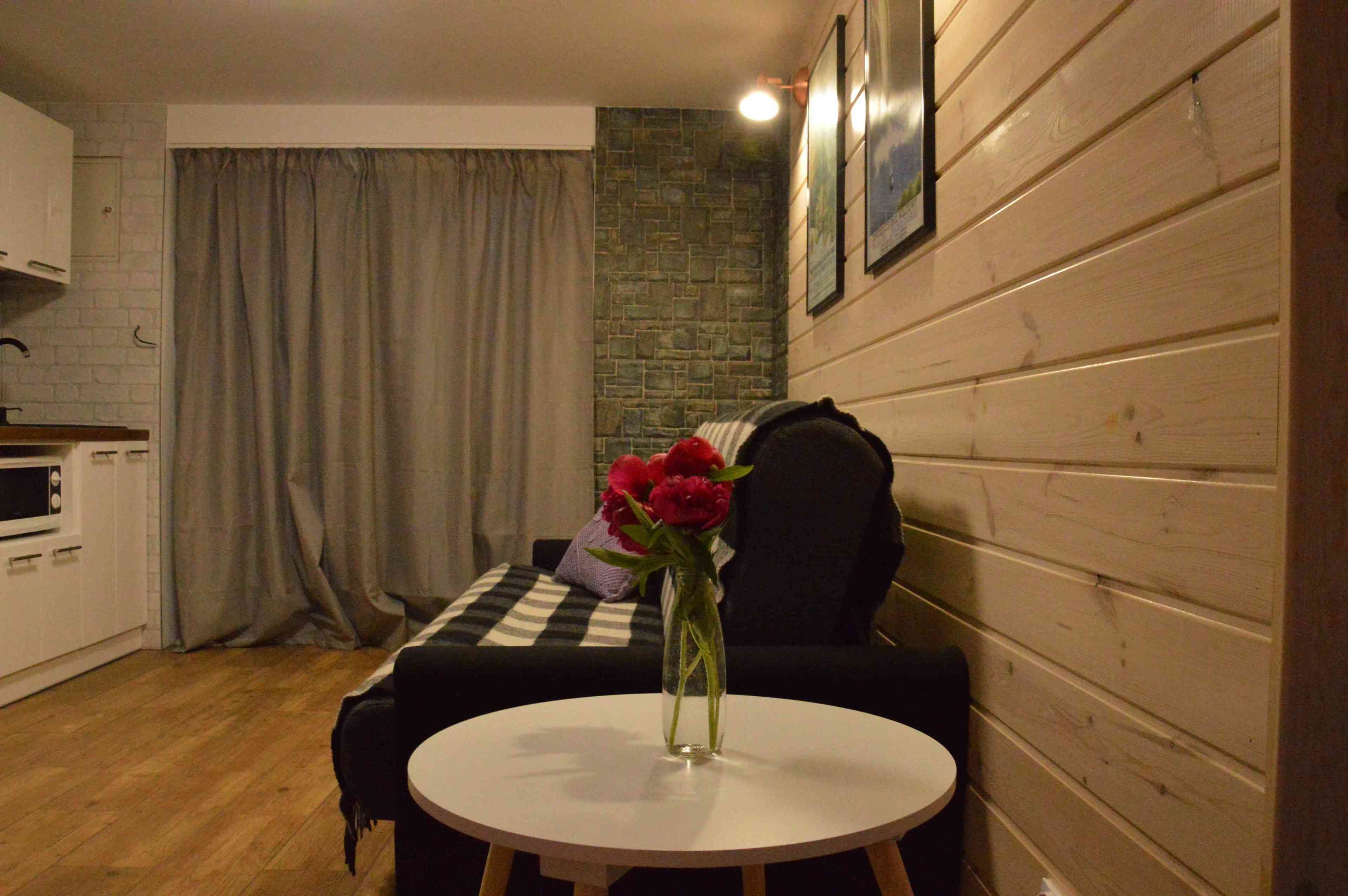 Una habitación acogedora con una mesa redonda, un sofá negro, un armario blanco y una pared de piedra.