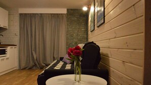 A cozy room with a round table, a black sofa, a white cabinet, and a stone wall. - Maryna House - Lawendowy Apartament (Zakopane)