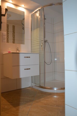 Ein modernes Badezimmer mit einer in Glas eingefassten Dusche, einem weißen Waschtisch mit Schubladen und einem Spiegel über dem Waschbecken.