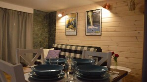 A dining area with a wooden wall, a checkered tablecloth, and a vase with red flowers. - Maryna House - Lawendowy Apartament (Zakopane)