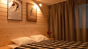A bedroom with a checkered bedspread, wooden walls, two framed posters, a nightstand with a vase of red flowers, and a window with curtains. - Maryna House - Lawendowy Apartament (Zakopane)