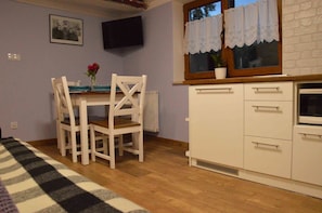 A small kitchen with white cabinets, a wooden countertop, and a window with lace curtains.