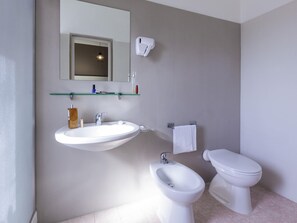 Ένα μπάνιο με νιπτήρα, μπιντέ, τουαλέτα και έναν καθρέφτη πάνω από τον νιπτήρα.