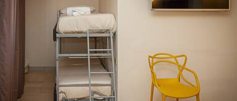 A bunk bed with a mattress and pillows, a yellow chair, and a window with lights.