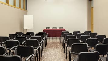 Een vergaderzaal met rijen stoelen gericht op een tafel met een rode tafelkleed.