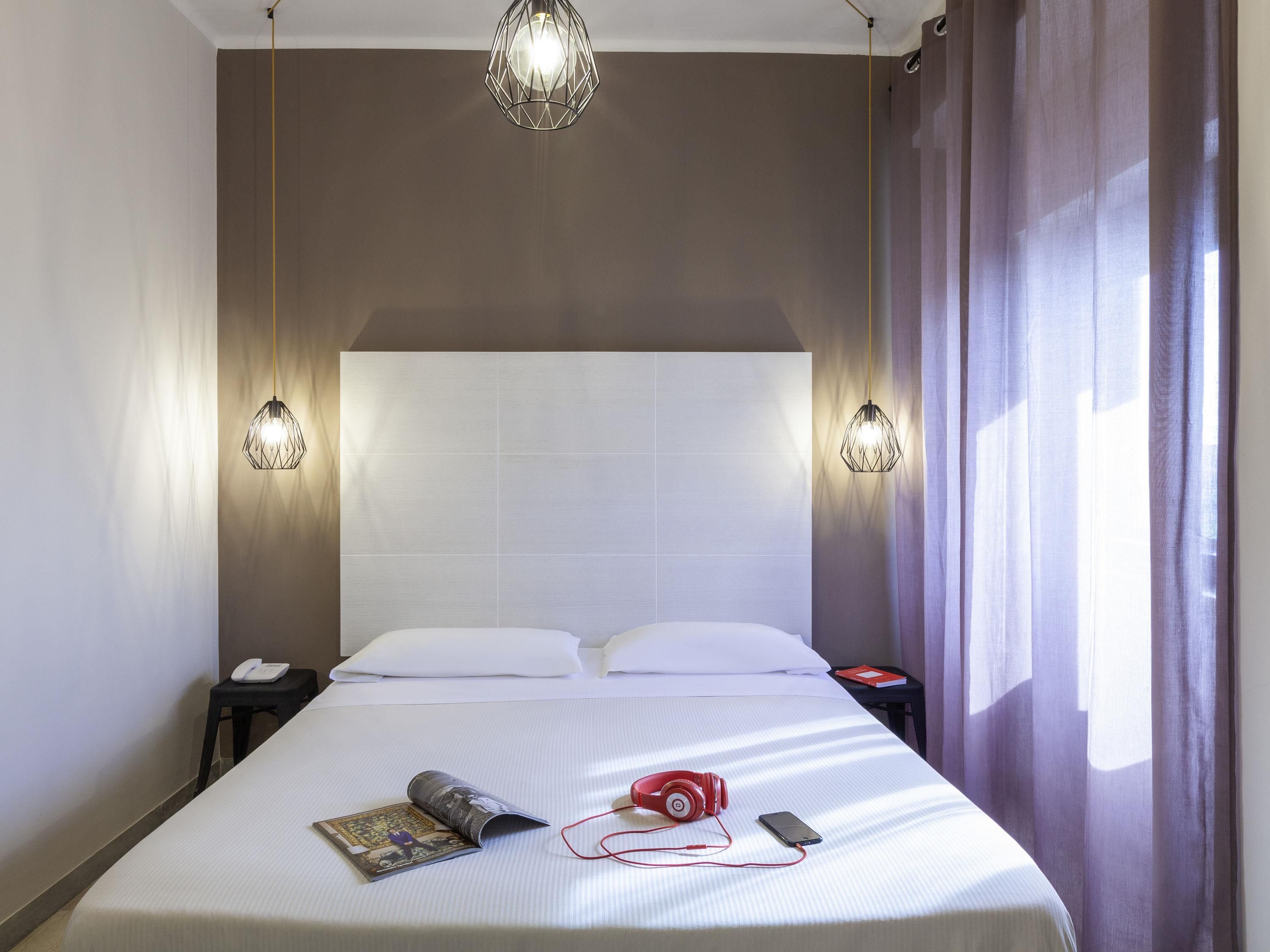 Ein Hotelzimmer mit einem großen Bett, zwei Nachttischen, einer Kopfteil und einem fenster mit Vorhängen.