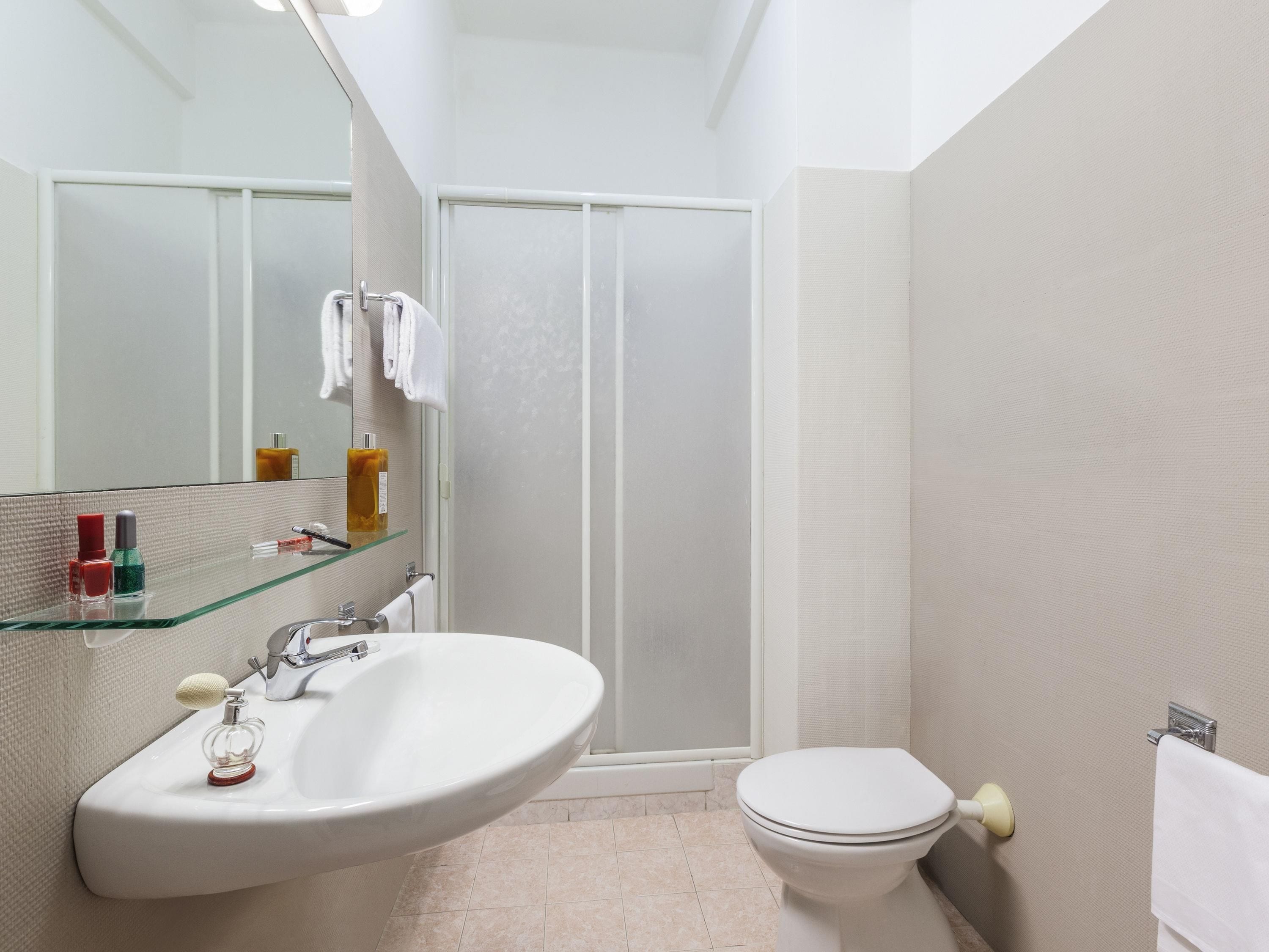 A bathroom with a glass-enclosed shower, a white sink with a soap dispenser, and a toilet.