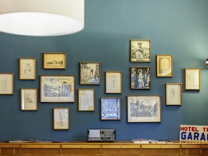 Una pared con múltiples obras de arte enmarcadas, un escritorio de madera con una radio, y un letrero que dice 'HOTEL TR'.