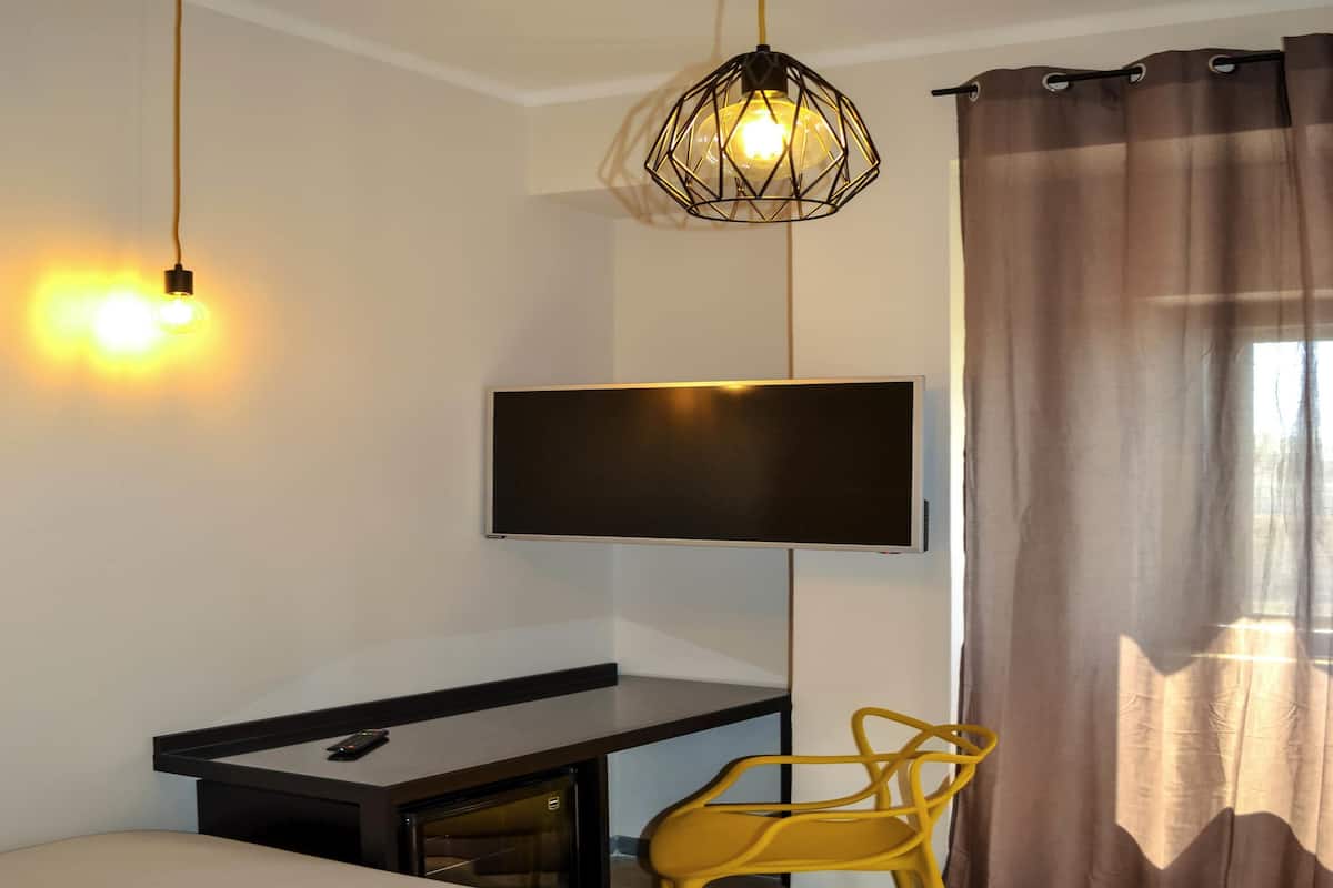 A modern room with a bed, a desk with a TV, a chair, and a hanging light fixture.