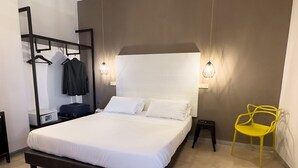 A modern bedroom with a large bed, a bedside table, a mirror, a hanging rack, and a yellow chair. - ibis styles Trani (Trani)