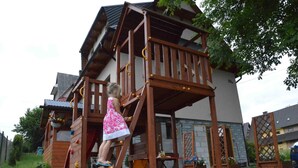 A wooden play structure with a slide and climbing elements, adjacent to a building with a stone facade and a metal roof. - Maryna House - Widokowy Apartament (Zakopane)