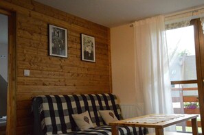 Ein gemütliches Zimmer mit Holzvertäfelung, einem karierten Sofa, zwei gerahmten Bildern an der Wand und einem Fenster mit Vorhängen.