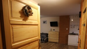 A wooden door with a wreath, a kitchen area with a TV, and a living space with a sofa and a coffee table. - Maryna House - Widokowy Apartament (Zakopane)