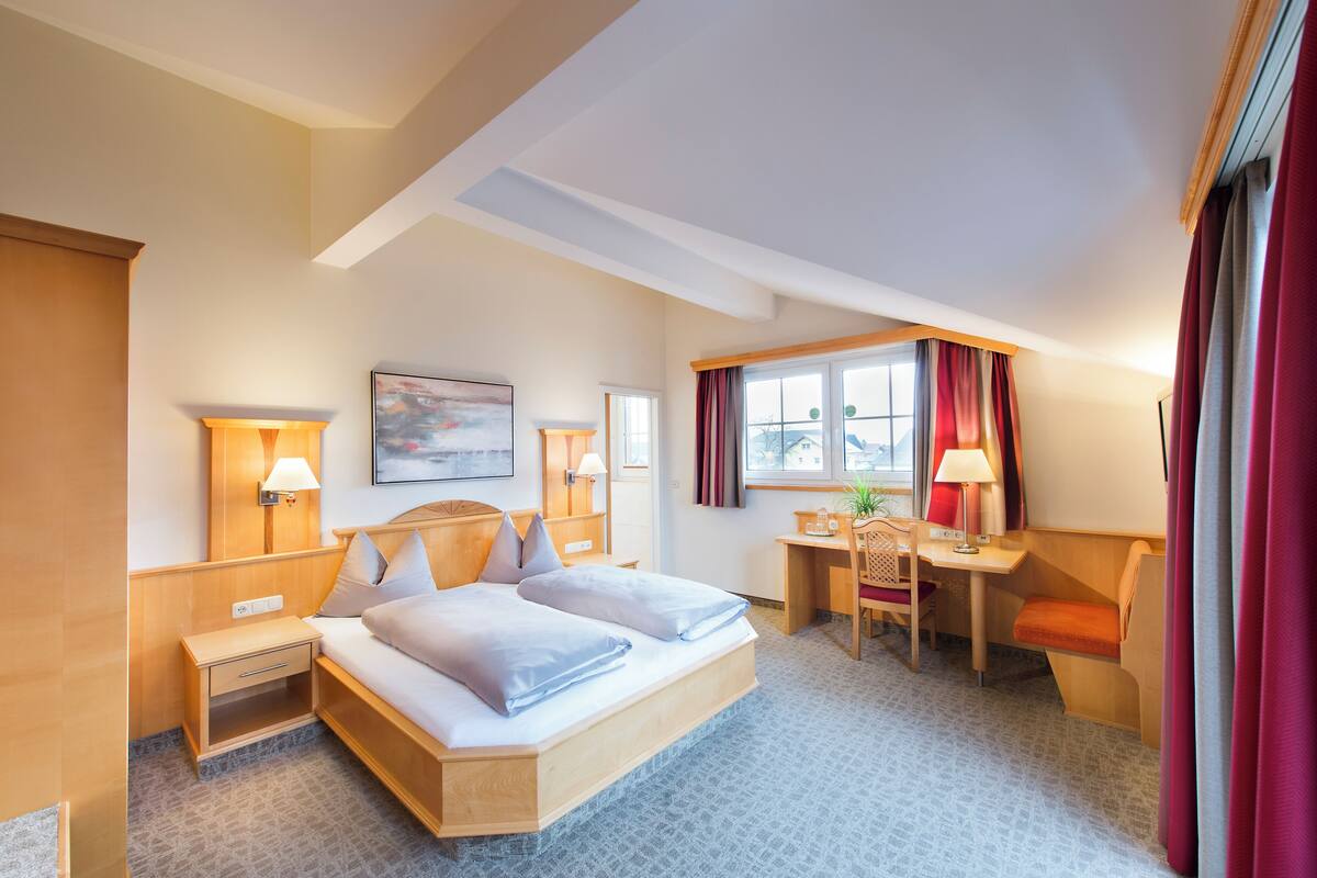 Habitación de hotel con cama, escritorio, silla, lámparas y un cuadro en la pared.