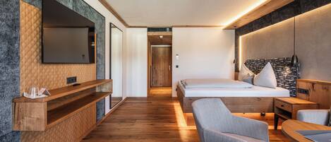A modern hotel room with a large bed, a desk, a chair, a TV, and a wooden floor.