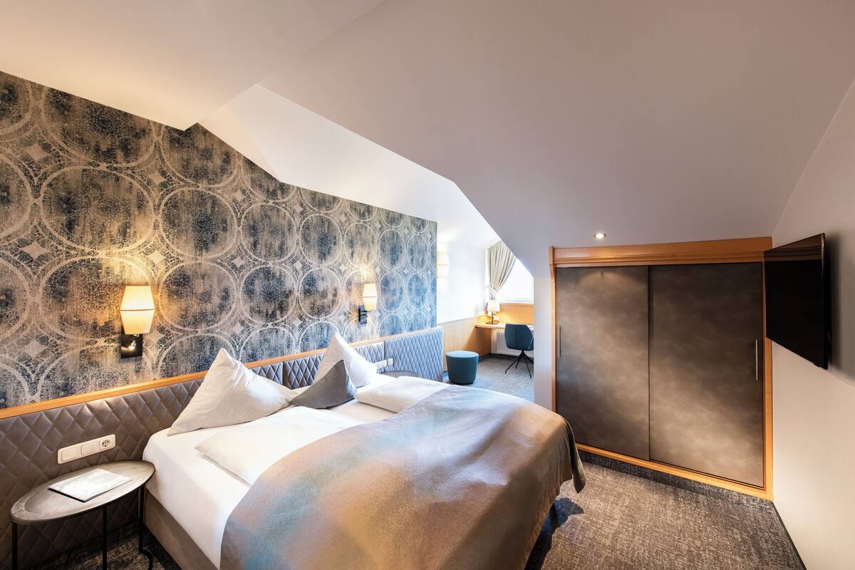 Una habitación de hotel moderna con una cama grande, una mesita redonda, un escritorio y un armario.