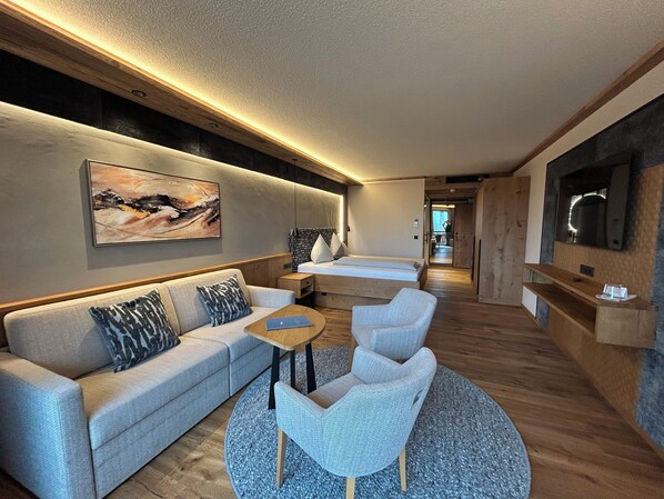 Habitación de hotel moderna con sofá, dos sillones, una mesita, cama y televisor.