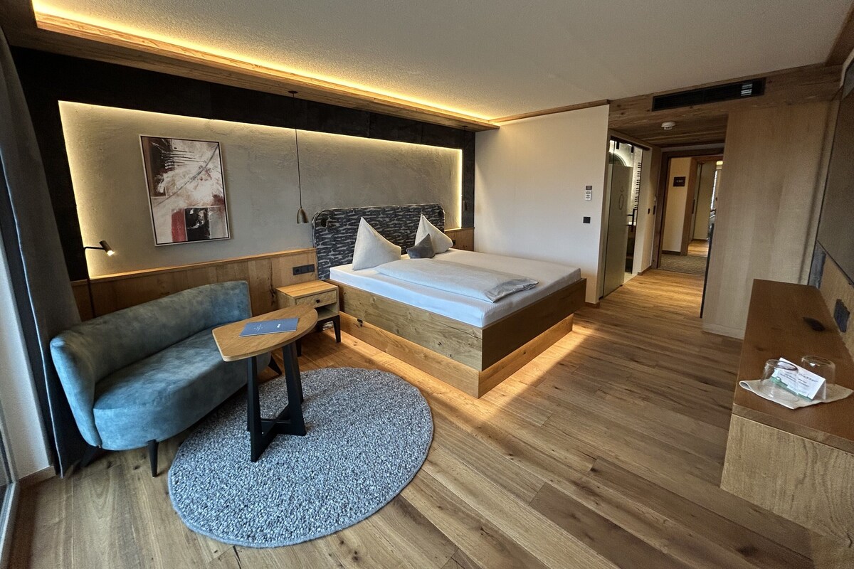 A modern hotel room with a wooden bed, a sofa, a small table, and a round rug.