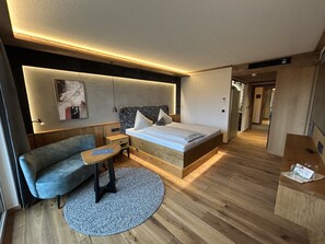 Una habitación de hotel moderna con una cama de madera, un sofá, una mesita y una alfombra redonda.