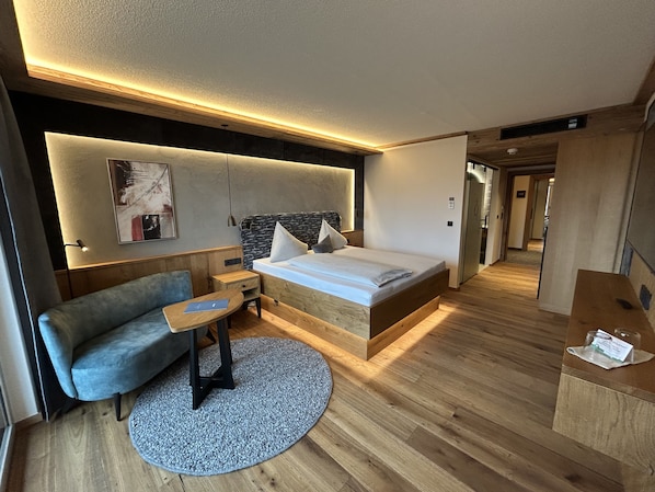 Ett modernt hotellrum med en säng i trä, en soffa, ett litet bord och en rund matta.