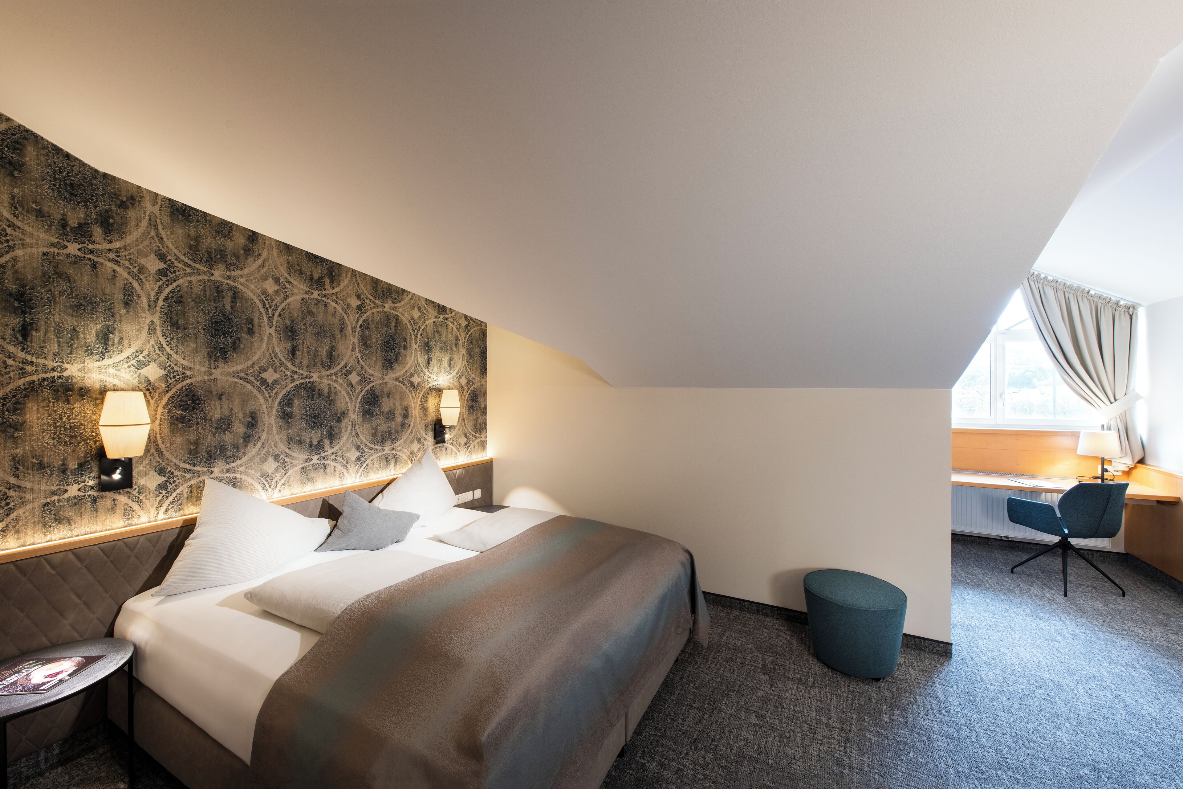 A hotel room with a bed, bedside lamps, a desk, and a chair.