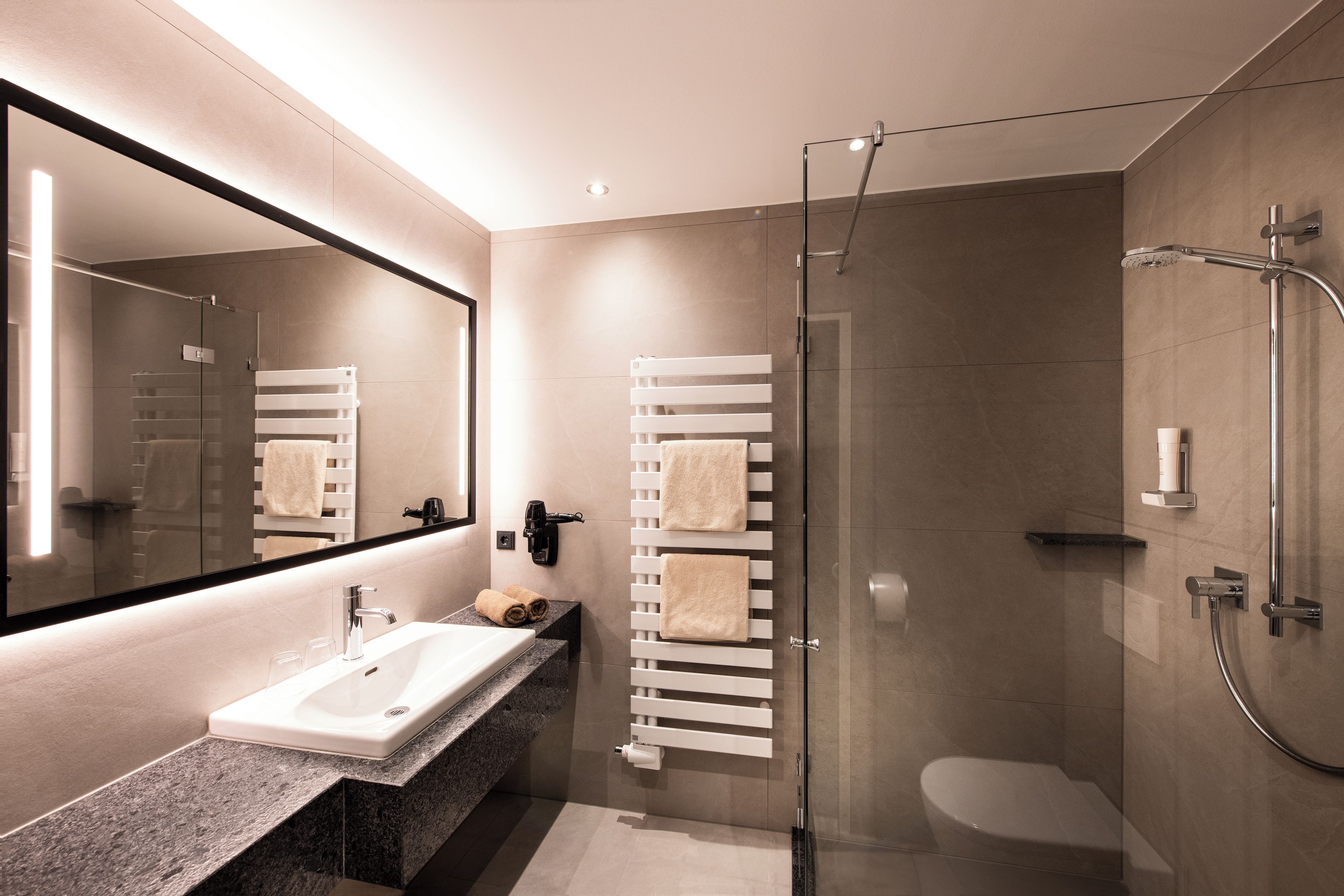 Een moderne badkamer met een glazen douchecabine, een wastafelmeubel en een handdoekrek.