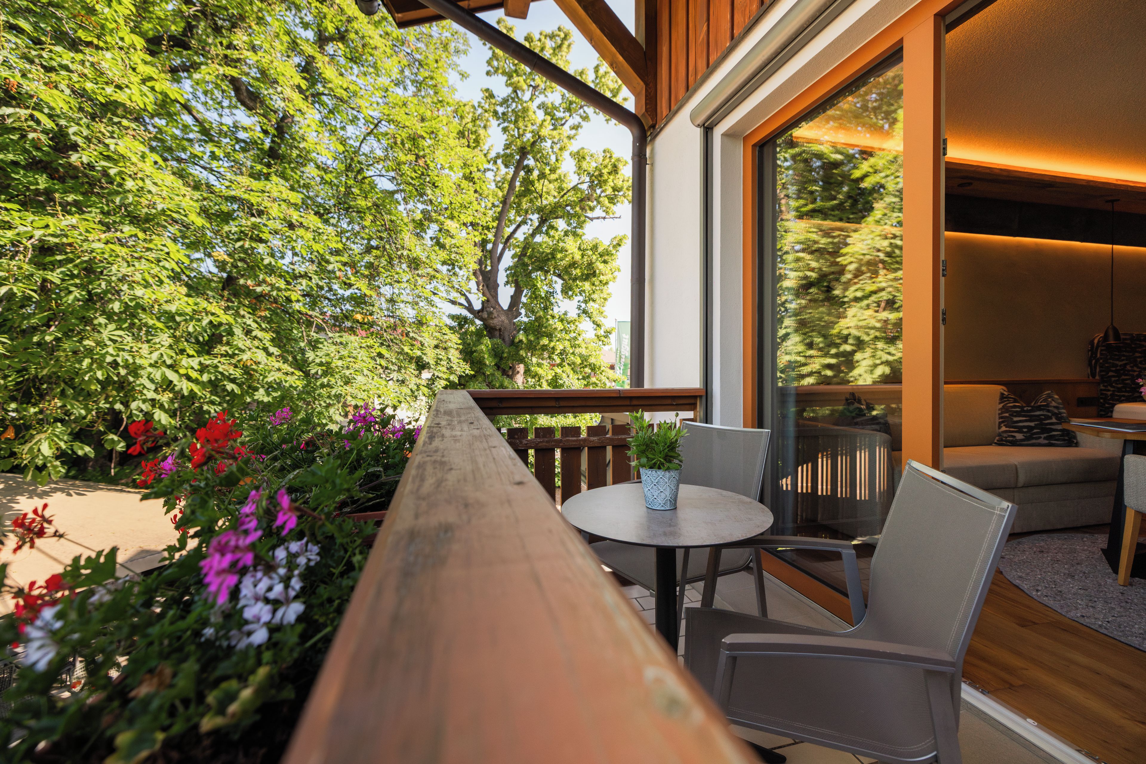 A wooden deck with a table and chairs, overlooking a garden with various plants and flowers.