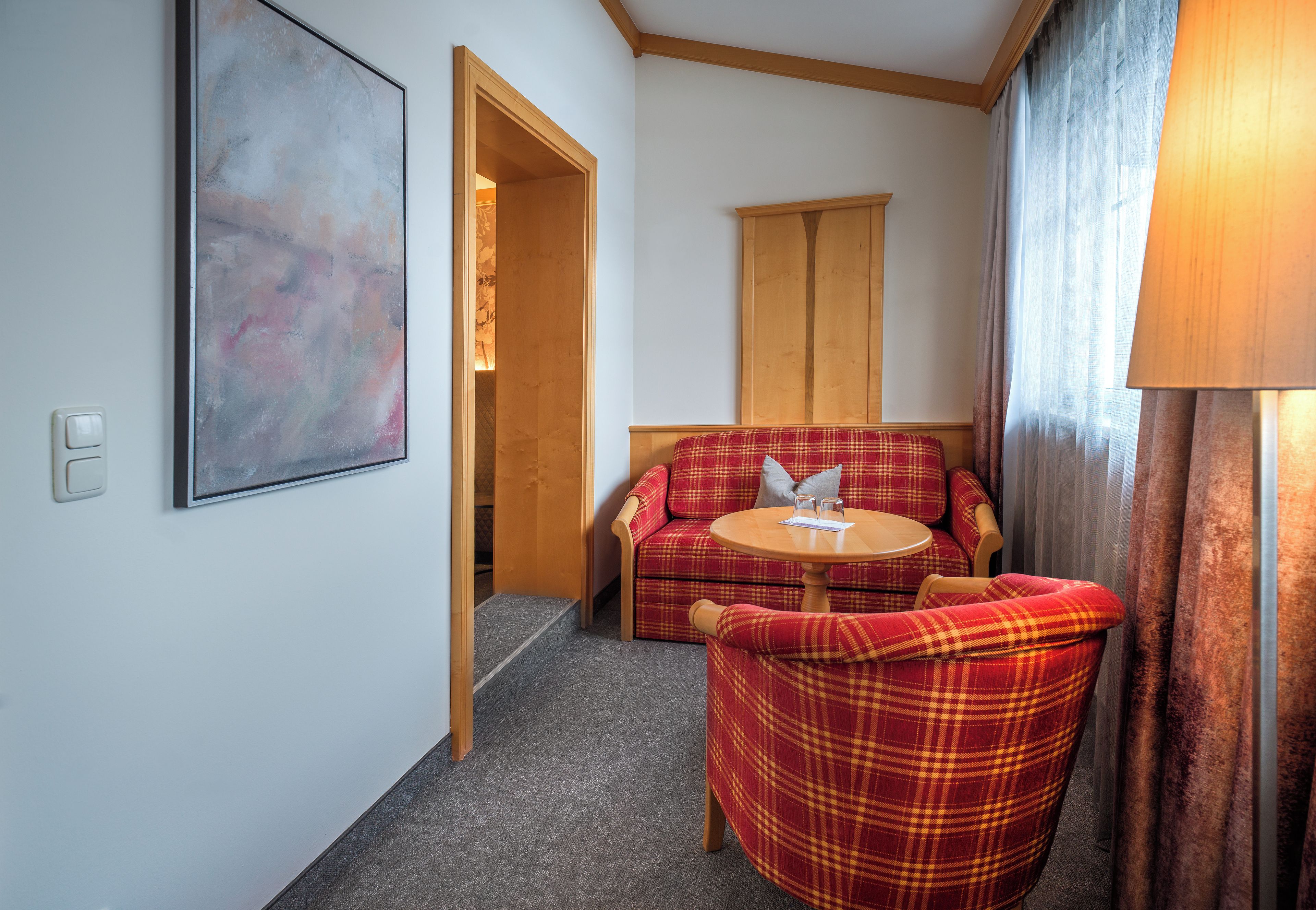 A hotel room with a plaid sofa, a small round table, a painting on the wall, and a wooden door.