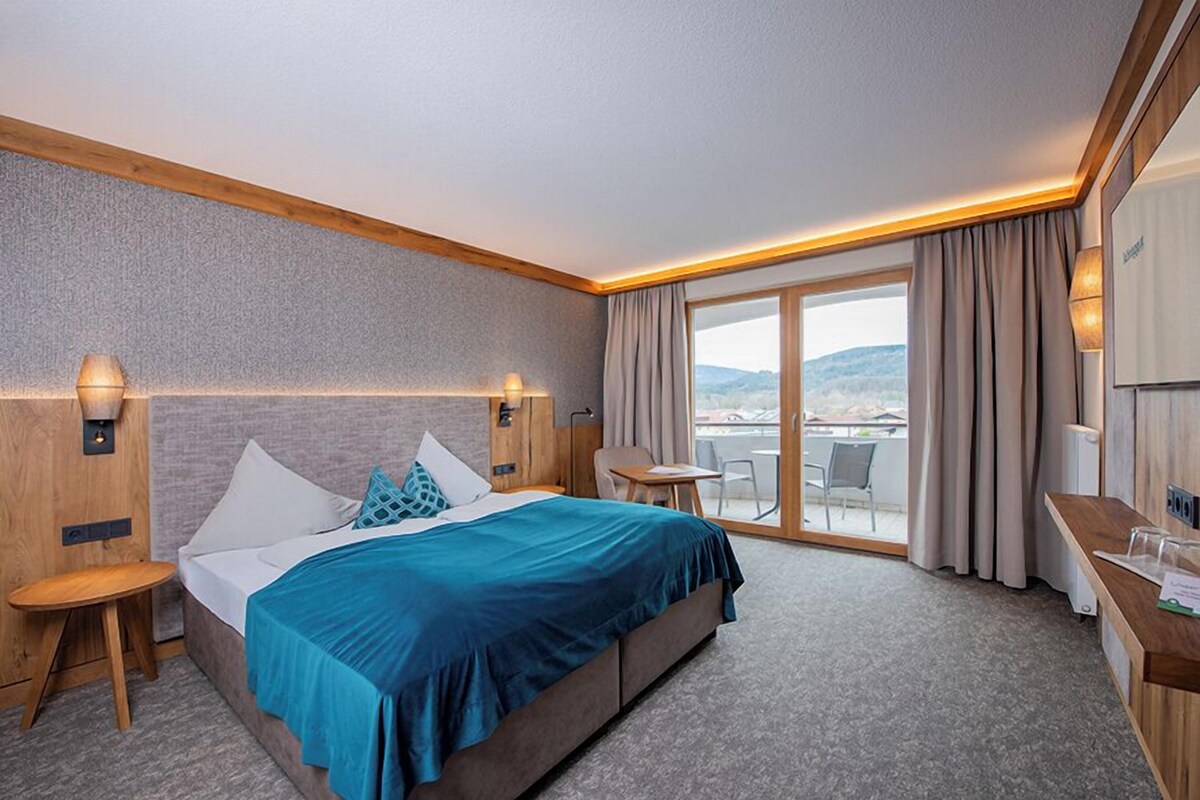 A hotel room with a large bed, a desk, a chair, and a view of the outdoors.