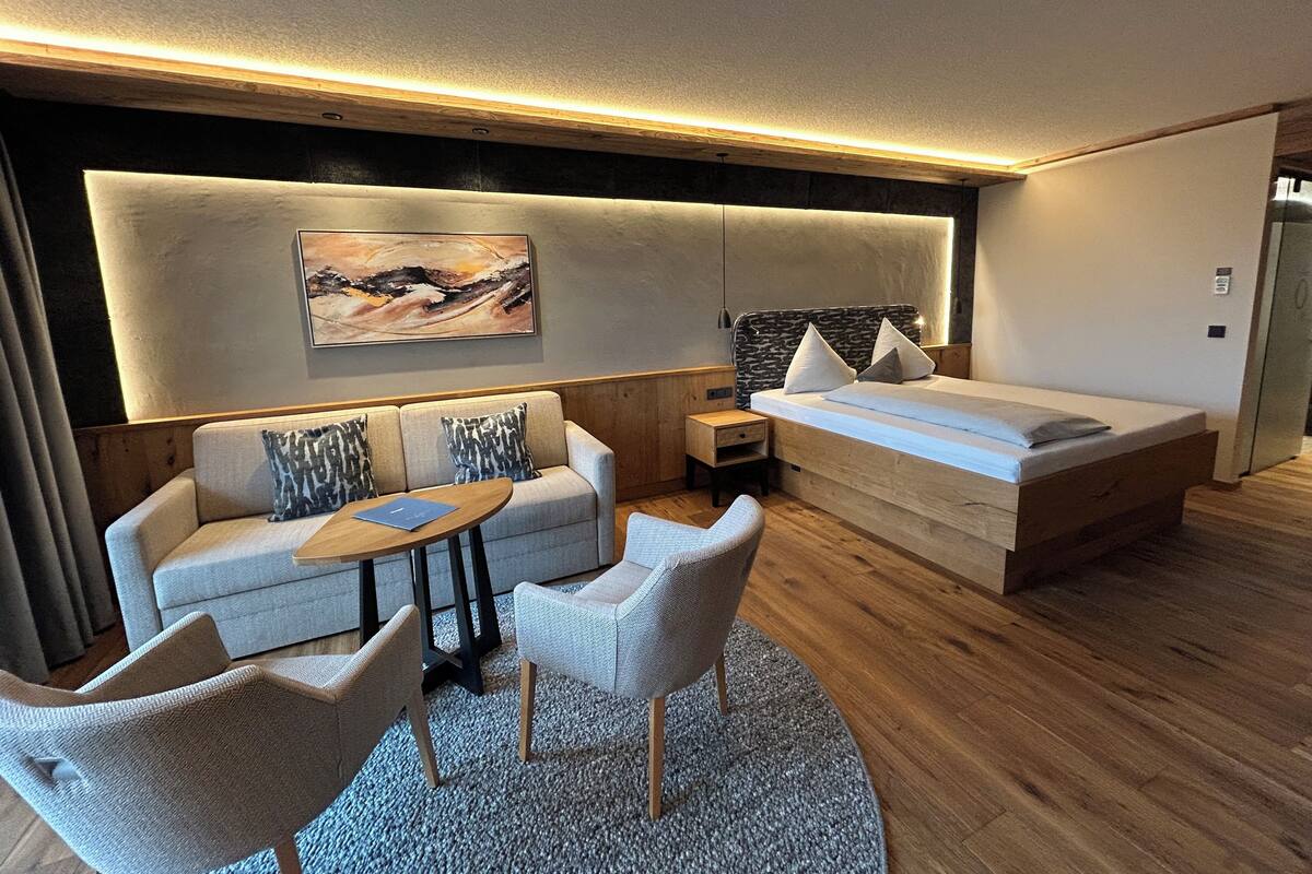 Habitación de hotel moderna con sofá, dos sillones, una mesita, cama y un cuadro en la pared.