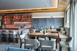 A modern bar area with a wooden ceiling, a seating area with a bench and chairs, and a bar counter with shelves of bottles. - Hotel Königgut (Wals-Siezenheim)