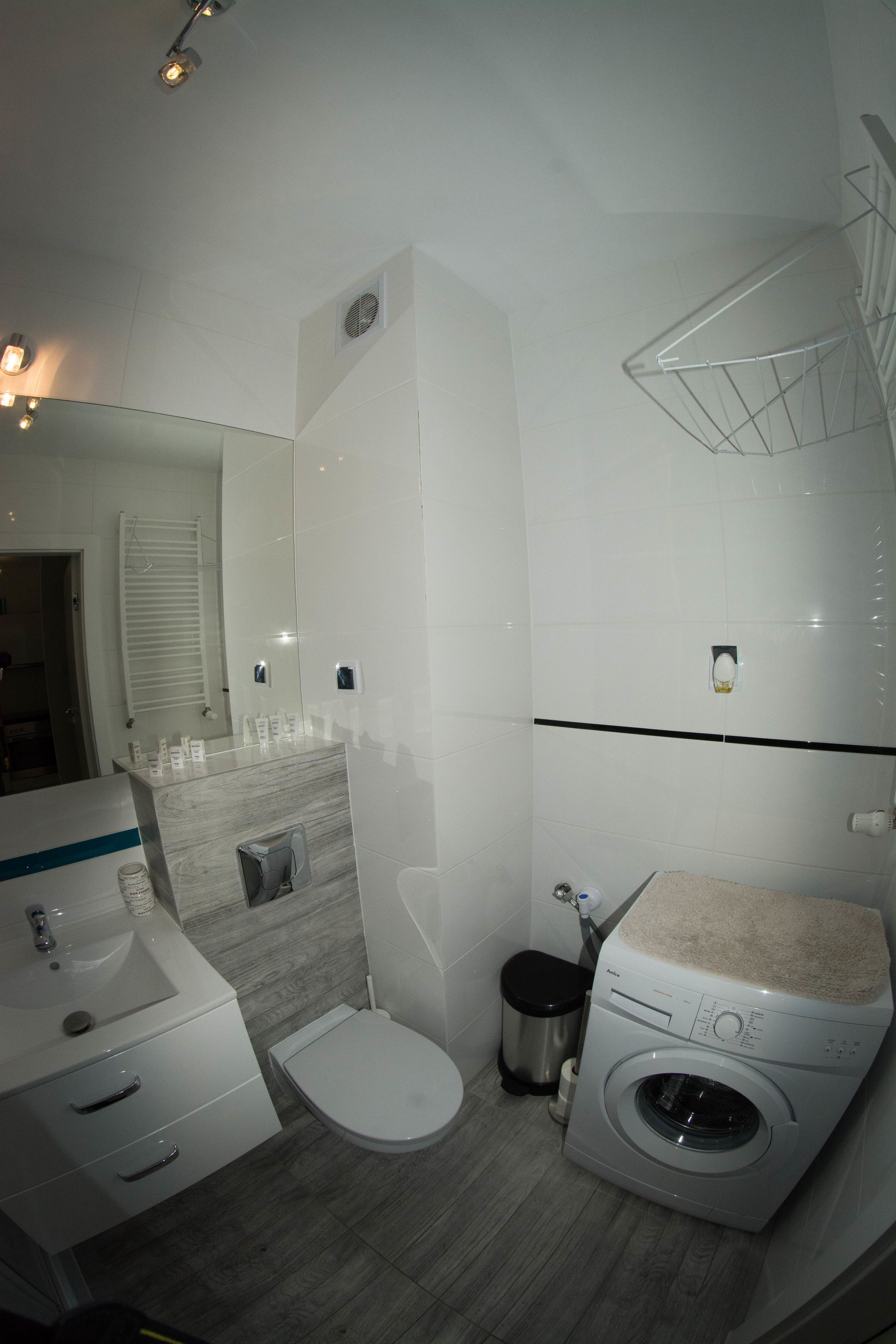 Ein modernes Badezimmer mit Waschbecken, Toilette und Waschmaschine, einem Spiegel und einem Handtuchhalter.